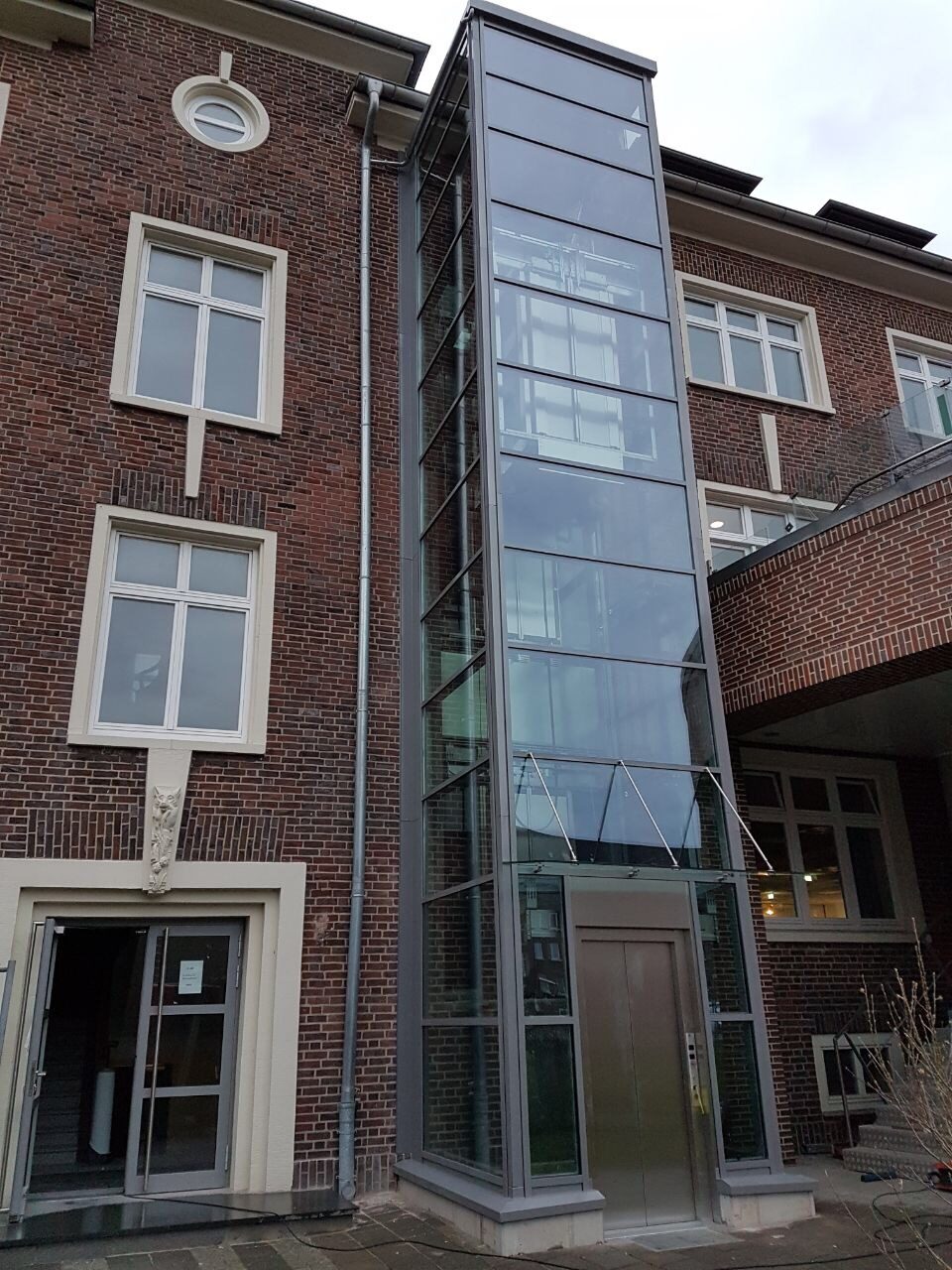 Aufzugsschachtgerüst aus Stahl und Glas vor einer Klinkerfassade in Bremerhaven